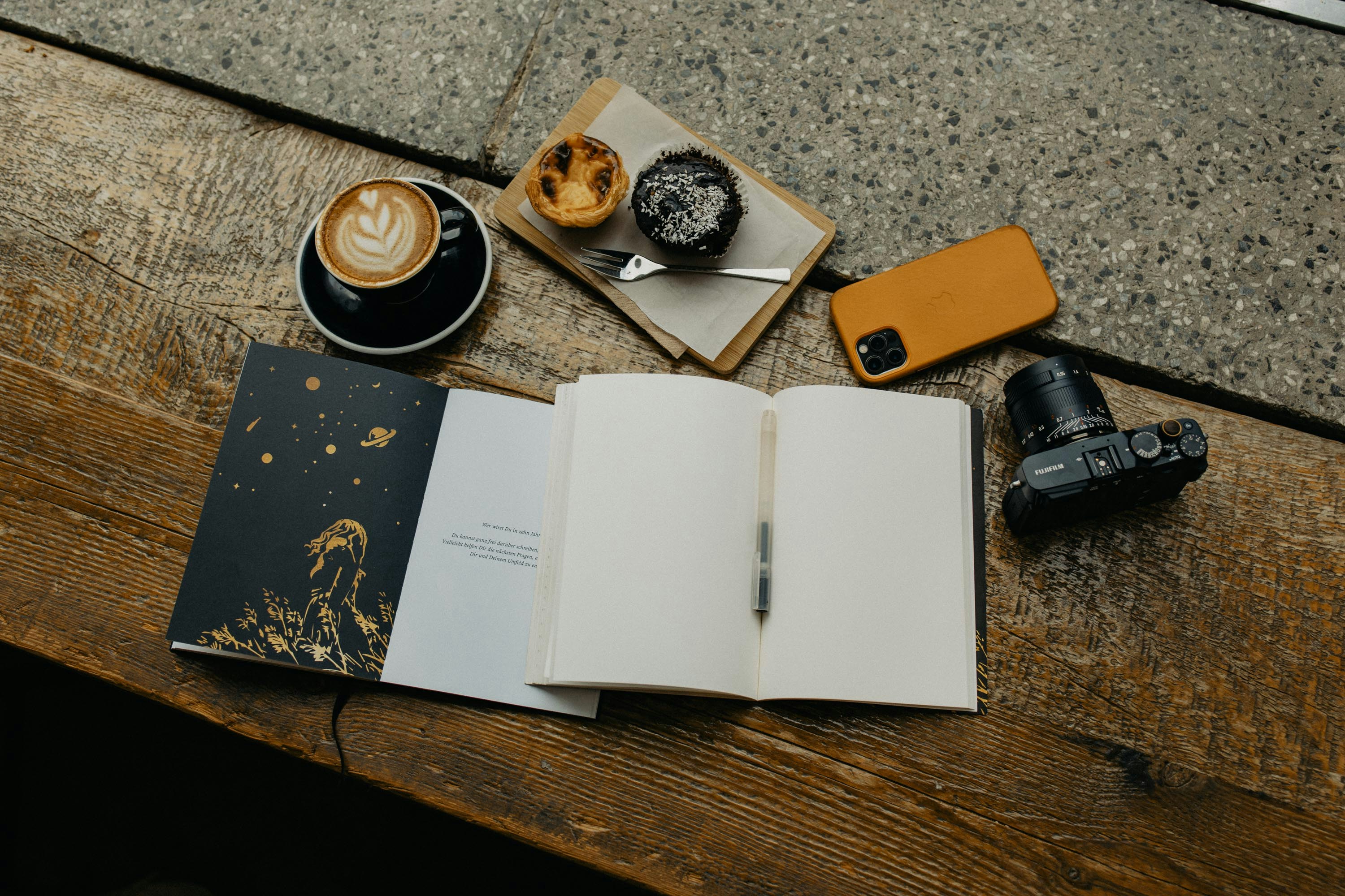 A person holding a smartphone face-down on a wooden table beside a book and a cup of coffee, representing a screen-free moment