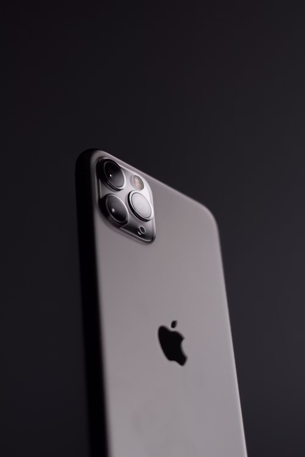 An older iPhone resting screen-down on a wooden desk next to a charging cable